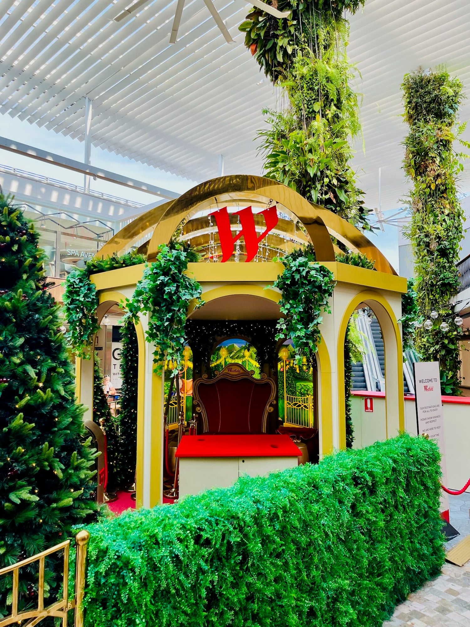 A Santa set in Westfield Warringah Shopping centre mall. Shows green foliage with LED fairy lights, a red Santa chair in the middle for photos